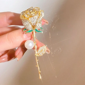 Detailed macro view of a golden rose brooch with rhinestones and a white pearl accent