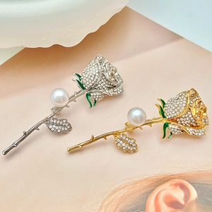 Macro detail of rose brooches with rhinestones, green enamel leaves and white pearls