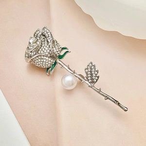 Close-up of rose brooch featuring white rhinestones, green enamel leaf, and large pearl