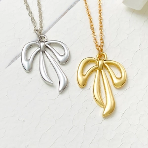 Nahaufnahme eleganter Schleifenanhänger in Gold und Silber auf feinen Ketten vor weißem Hintergrund