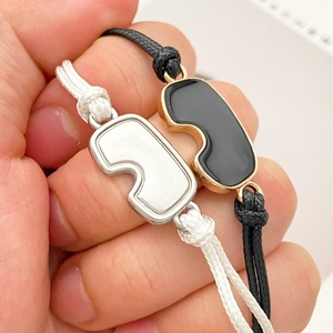 Primer plano de pulseras de pareja tejidas en blanco y negro con colgantes abstractos