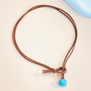 Detail of square turquoise stone pendant with silver frame on brown cord necklace