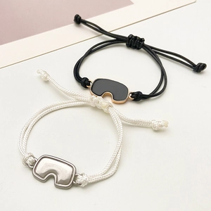 Detalle de pulseras trenzadas ajustables para pareja con colgantes de metal únicos