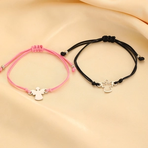 Detalle de pulseras ajustables con dije de ángel para parejas sobre fondo de seda amarilla