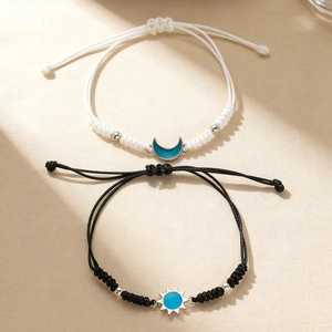 Primer plano de pulseras tejidas para parejas con colgantes de sol y luna sobre fondo