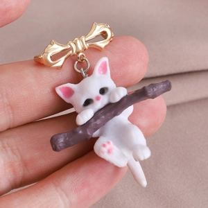 Broche chat minimaliste avec nœud doré et détails roses sur une branche brune