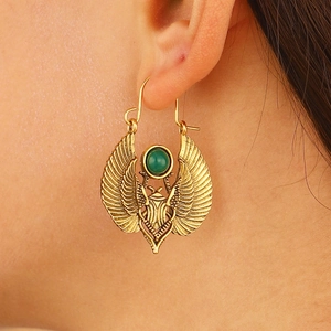 Close-up of Egyptian gold scarab earrings with green gemstone on model