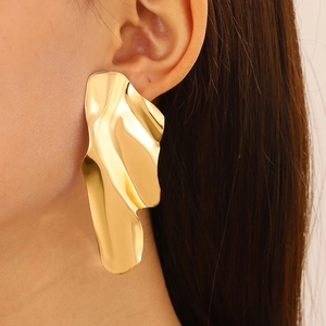 Close-up of oversized gold wavy earrings with irregular polished metallic texture