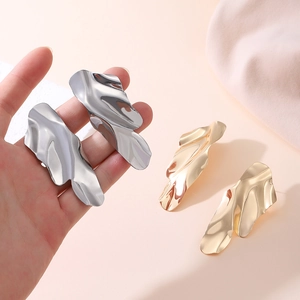 Detailed close-up of oversized irregular wave-shaped metal earrings in gold and silver