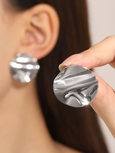 Close-up of irregular textured silver metal earrings worn by a model in a minimal style