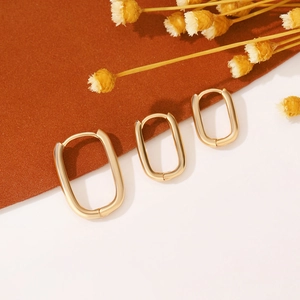 Dettaglio di tre orecchini a cerchio rettangolari in oro opaco minimalisti su sfondo estetico