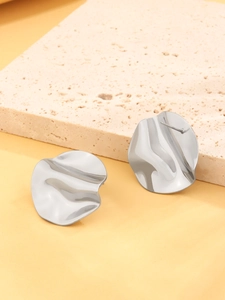 Macro detail of irregular silver geometric metal stud earrings on a textured stone surface