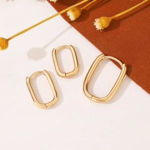 Tre orecchini a cerchio geometrici minimalisti in oro opaco su sfondo bianco e marrone