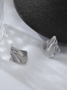 Detail macro shot of silver irregular wave square stud earrings with high-polish finish