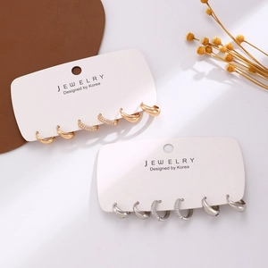 Dettaglio di set di orecchini a cerchio minimalisti in oro e argento con zirconi su carte