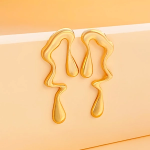 Close-up of golden liquid metal earrings with irregular molten drop design on stand