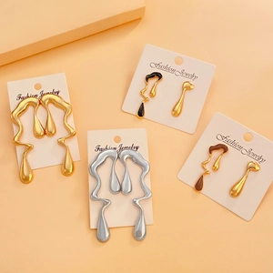 Flat lay of irregular liquid-style gold and silver earrings with enamel details on orange background