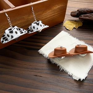 Close-up of creative cowboy hat earrings with cow print and brown texture hanging on wood