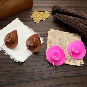 Disco ball earrings with cowboy hat charms in brown and pink on rustic wood background