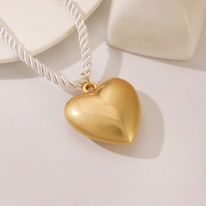 Detail shot of a polished gold puffy heart pendant on a white twisted rope chain
