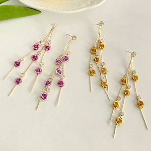 Macro detail of long gold tassel earrings with colorful metal roses and sparkling crystals