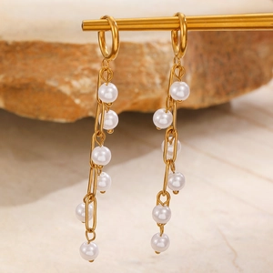 Detail of long gold pearl tassel earrings hanging on a display stand with rock background