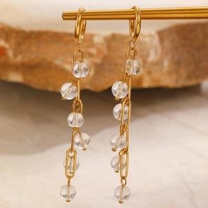 Detail view of long gold tassel earrings with clear beads on a marble background