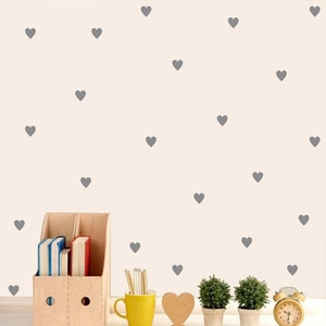 Detail of small grey heart wall stickers scattered on a warm beige wall surface