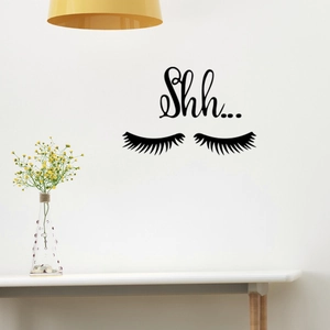 Detail of creative eyelash wall decal with Shh text on white wall with yellow lamp