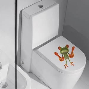 Detail view of a 3D cartoon green frog sticker applied to a modern white toilet lid
