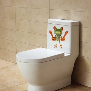 Funny green frog sticker with red eyes applied on a white ceramic toilet tank surface