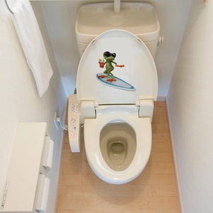 Close-up of funny surfing cartoon frog waterproof sticker applied on a white toilet lid