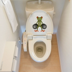 Macro shot of a funny 3D green frog lifting weights on a white toilet lid decal
