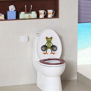 Funny 3D green frog lifting weights sticker on a white ceramic toilet lid in a bathroom