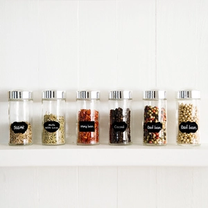 Set of six glass kitchen jars with silver lids and black chalkboard labels for food storage