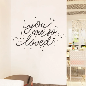 Détail du sticker mural You Are So Loved avec étoiles et pois sur un mur blanc de salon