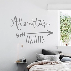 Detail of gray Adventure AWAITS wall decal with arrow on a clean modern bedroom wall