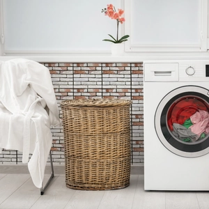 Large wicker laundry basket with lid set against a rustic red brick texture wall