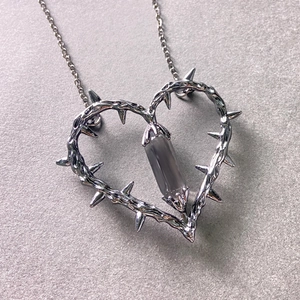 Macro detail of silver thorn heart pendant with grey crystal pillar on a metal chain