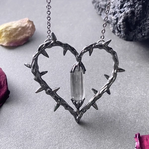 Detail of gothic thorn heart pendant with crystal on dark stone and flower petals