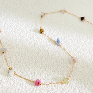 Detailaufnahme einer zarten Goldkette mit bunten, unregelmäßigen Edelsteinen