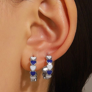Close-up of a model wearing heart-shaped enamel hoop earrings in blue and white