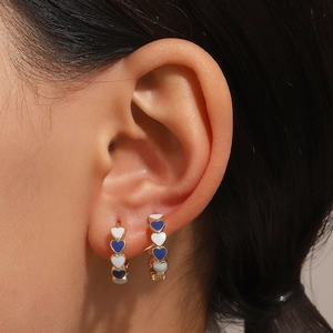 Close-up of heart enamel hoop earrings in blue and white on model ear for display