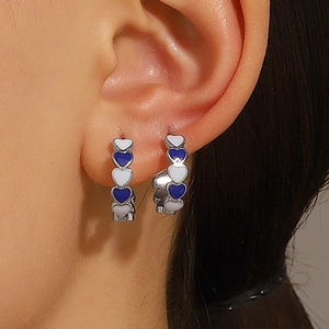 Close-up of C-shaped earrings with alternating blue and white enamel hearts on model
