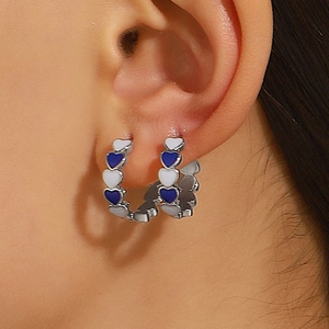 Close-up of blue and white heart enamel hoop earrings on model for a trendy summer look