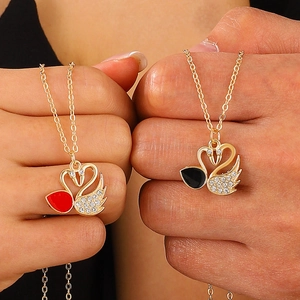 Close-up of gold swan necklaces with red and black enamel inlay and sparkling crystals