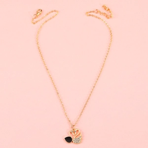Macro detail of gold twin swan pendant with crystal pavé and black enamel finish