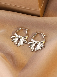 Macro shot of silver bow earrings with heart center on golden satin fabric background
