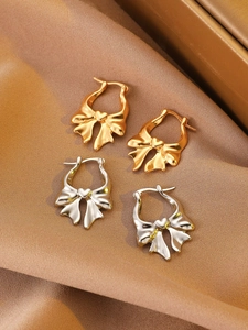 Detailed macro shot of gold and silver bow heart earrings on elegant brown silk fabric