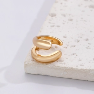 Close-up of minimalist gold ear cuff with polished finish on a white stone pedestal